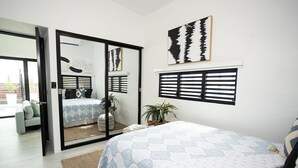 A bedroom with a bed, a sliding glass door leading to a balcony, a window with shutters, and a wall-mounted artwork. - Luxury Villa with private pool, Steps away from Black Eagle Beach (Rincón)