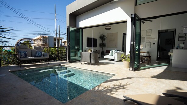 A modern house with a swimming pool, outdoor seating, and a glass door leading to a living area. - Luxury Villa with private pool, Steps away from Black Eagle Beach (Rincón)