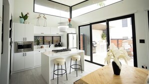 A modern kitchen with white cabinetry, a central island with bar stools, a built-in microwave, and a large sliding glass door leading to an outdoor area. - Luxury Villa with private pool, Steps away from Black Eagle Beach (Rincón)