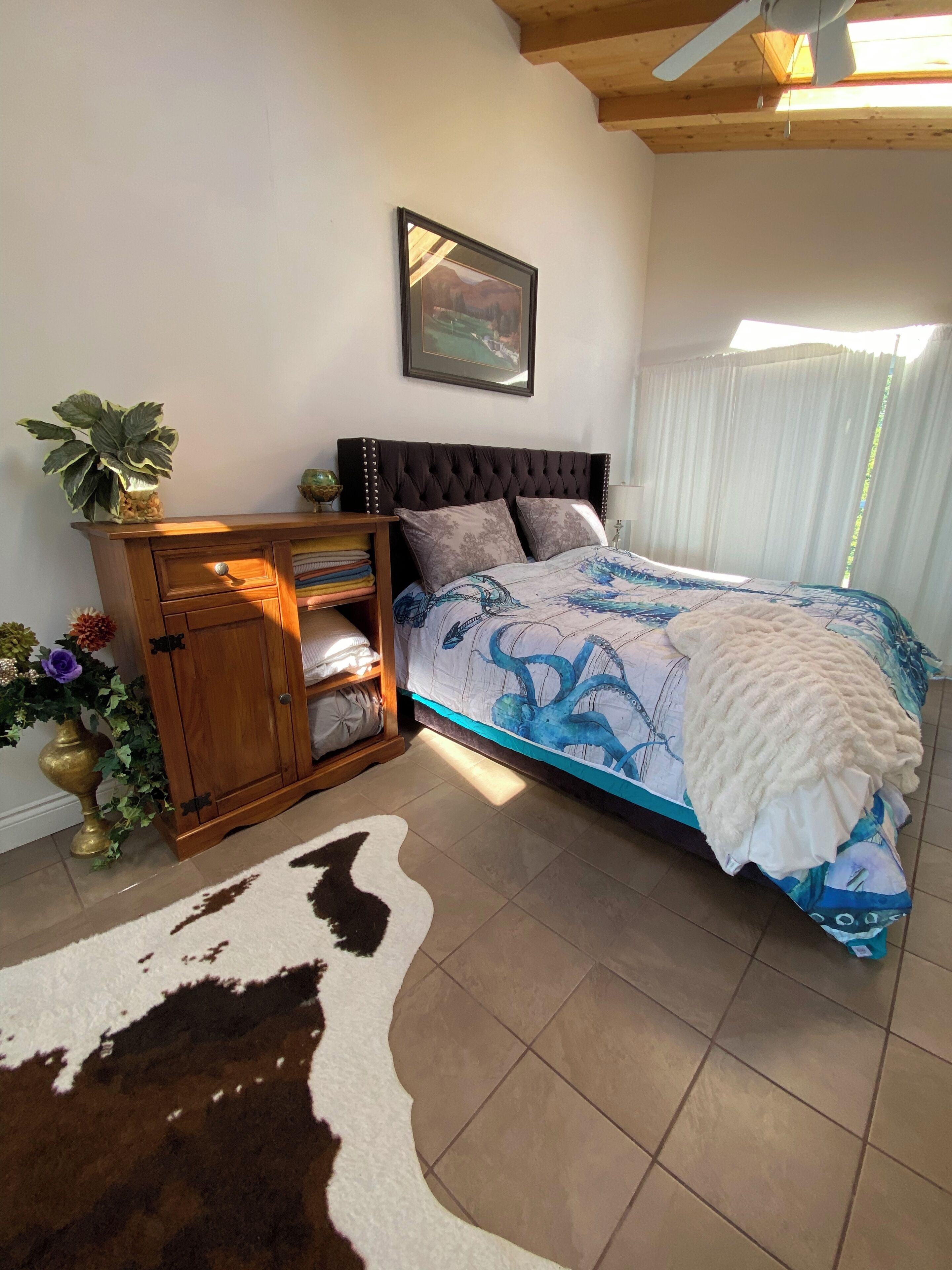 Un dormitorio con cama, un armario de madera, un tapete de piel de vaca y un ventilador de techo.