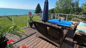 Eine Holzterrasse mit Korbmöbeln, einem blauen Tisch und Blick aufs Meer.
