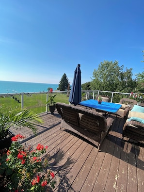 A wooden deck with wicker furniture, a blue table, and a view of the sea. - Huron waterfront cottage/Hot tub/max2 pets for16+people with private sand beach  (Goderich)