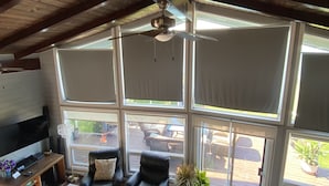 A spacious living room with a high ceiling, large windows, a ceiling fan, a flat-screen TV, a coffee table, and a seating area with two chairs. - Huron waterfront cottage/Hot tub/max2 pets for16+people with private sand beach  (Goderich)