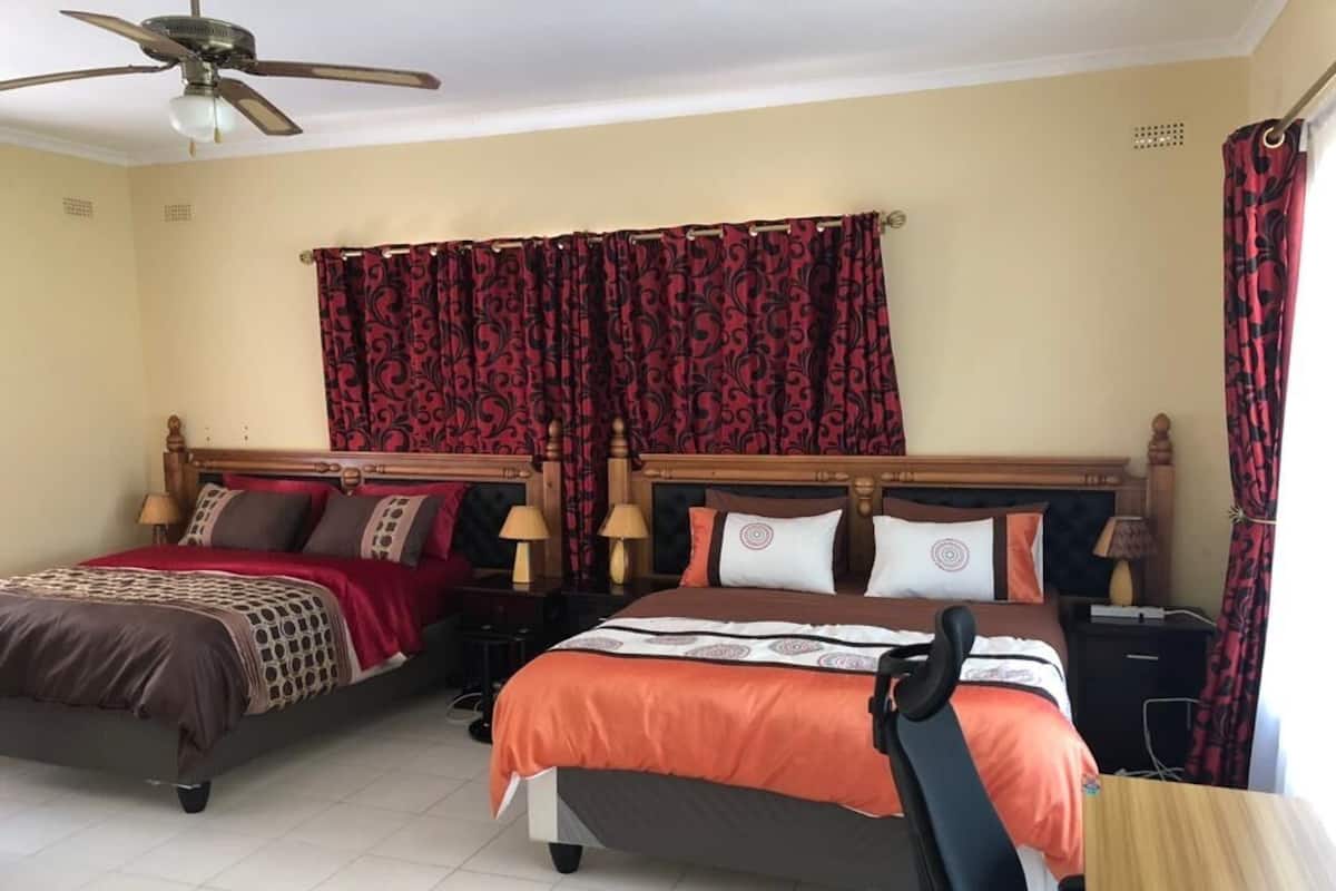 Une chambre d’hôtel avec deux lits, un ventilateur de plafond et des rideaux à motifs rouges.