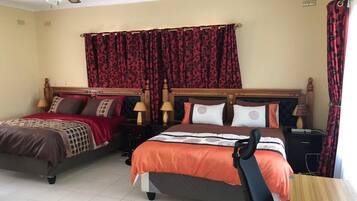 Habitación de hotel con dos camas, ventilador de techo y cortinas rojas con estampado.