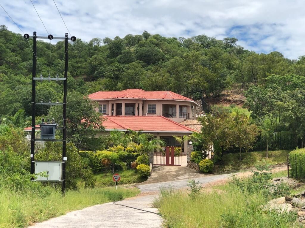 A house with a red roof, surrounded by lush greenery and a hill in the background.