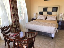Un dormitorio con cama, mesitas de noche, una silla, una mesa y cortinas.