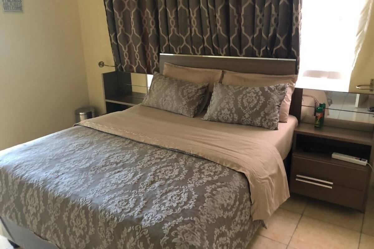 Un lit bien fait, recouvert d’une couvre-lit à motifs, une table de chevet avec une lampe et un miroir accroché au mur.