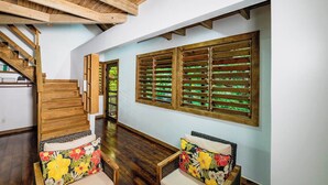 A spacious hallway with wooden flooring, a staircase, and two wicker chairs with floral cushions. - Hottest Sparrow - Charming Cottage (West End)