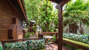 A wooden deck with a bench and a table, surrounded by lush greenery. - Hottest Sparrow - Charming Cottage (West End)