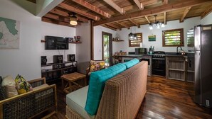A rustic kitchen with wooden beams, a dining area with wicker furniture, and a TV mounted on the wall. - Hottest Sparrow - Charming Cottage (West End)