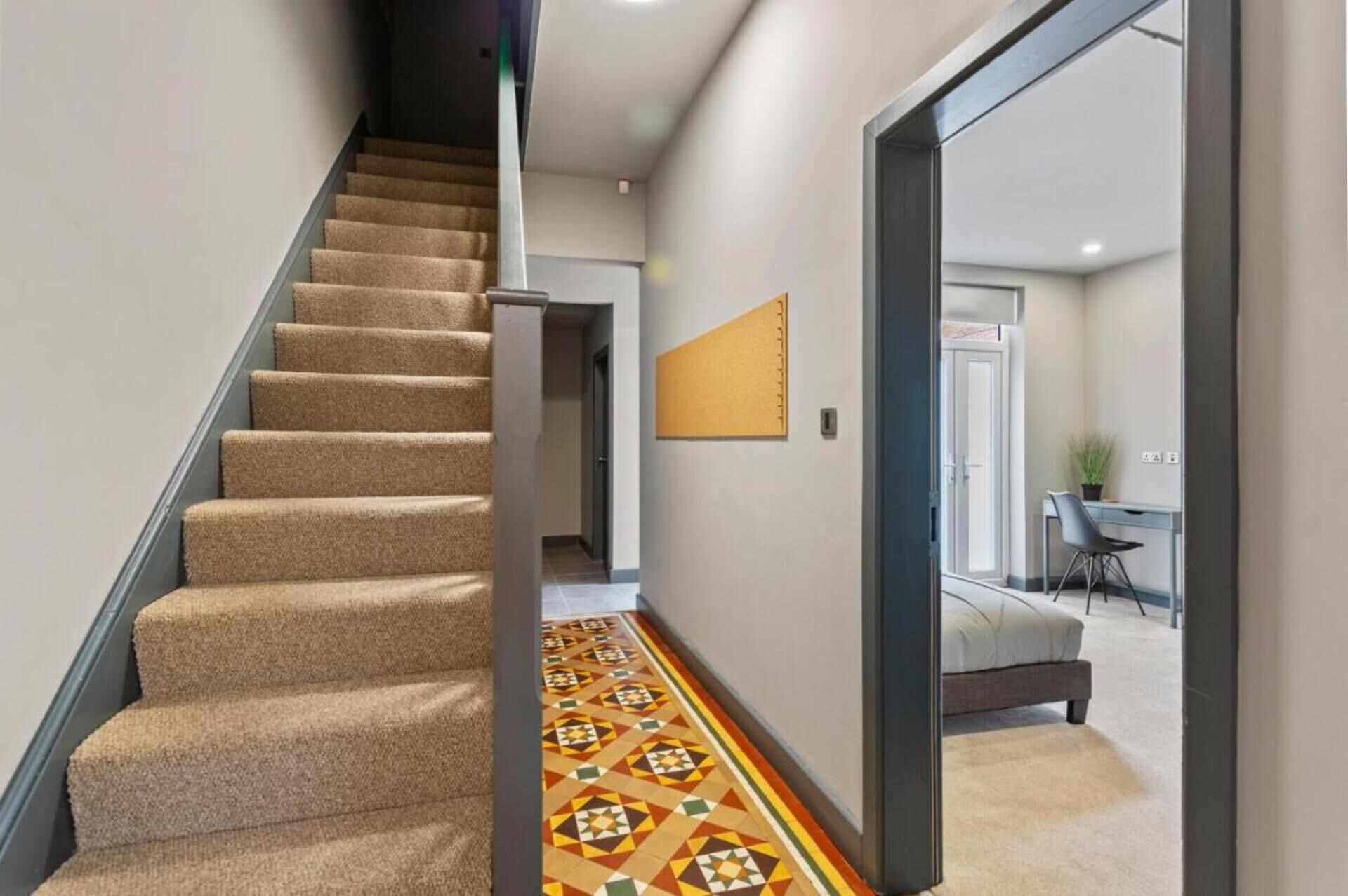 A staircase with carpeted steps leading to a room with a patterned floor.