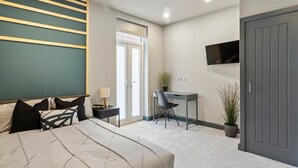 Une chambre à coucher moderne avec un lit, un bureau, une chaise, un téléviseur et une porte.