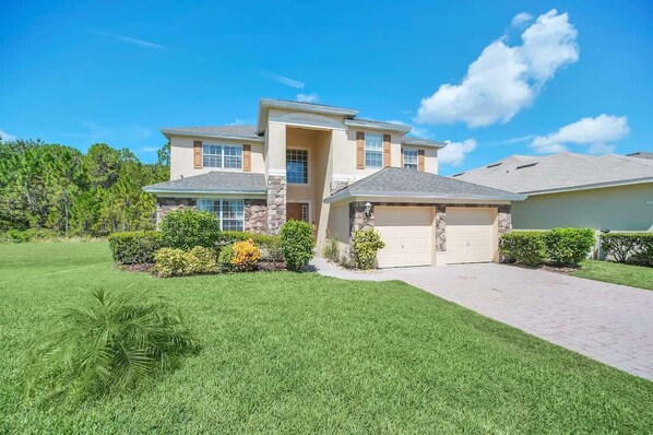 A two-story house with a garage, stone accents, and a well-maintained lawn. - Near Disney Amazing 5 Bd Home - Private Pool (Davenport)