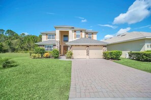 A two-story house with a garage, a paved driveway, and well-maintained landscaping. - Near Disney Amazing 5 Bd Home - Private Pool (Davenport)