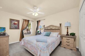 A bedroom with a bed, a nightstand, a desk, a ceiling fan, and a window with curtains. - Near Disney Amazing 5 Bd Home - Private Pool (Davenport)