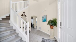 A staircase with white railings leading to an upper floor, a hallway with a tiled floor, a door with a white frame, and a potted plant.