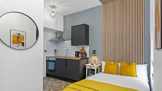 A modern hotel room with a bed, a bedside table, a lamp, and a view of the kitchen. - Studio 2 in Nottingham (Nottingham)