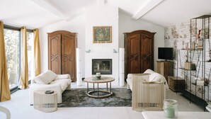 A spacious living room with two white sofas, a round coffee table, and a fireplace. There are large wooden cabinets and a bookshelf with books and decorative items. - The Aviary - Pernes-les-Fontaines (Pernes-les-Fontaines)