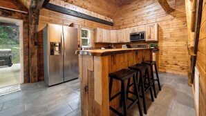 Une cuisine rustique aménagée dans une cabane en bois, équipée d’un réfrigérateur, d’un four à micro-ondes et de tabourets de bar.