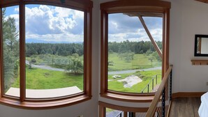 A room with two large windows offering a view of a green landscape with trees and a road. - Enjoy whatever winter throws at you while you relax in the hot tub with a view! (Vermontville)