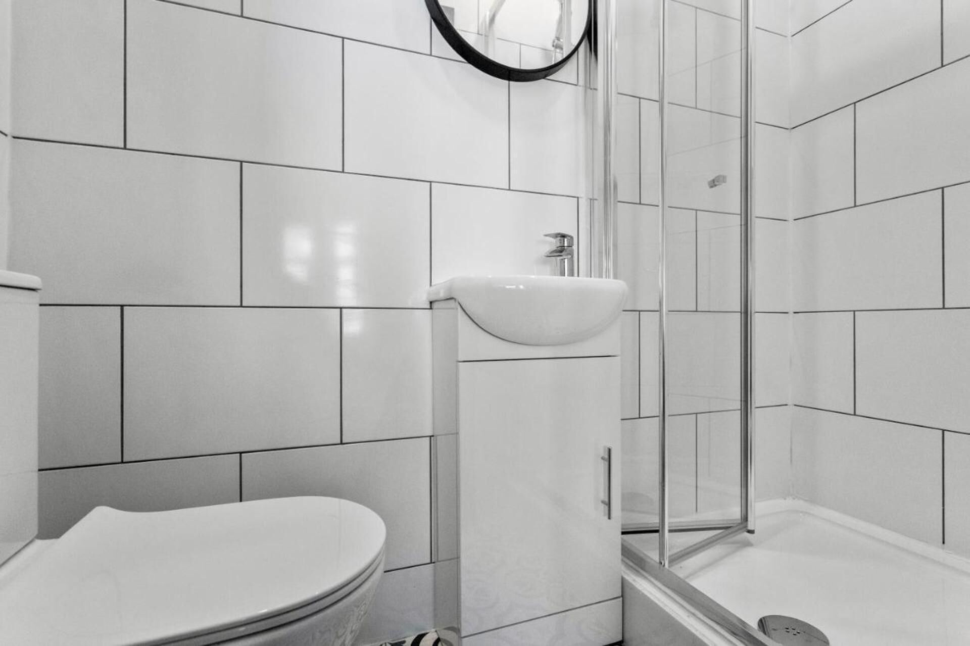 Een moderne badkamer met witte tegels, een toilet, een wastafel en een douchecabine van glas.