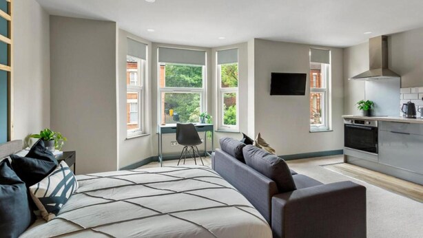 A modern bedroom with a large bed, a desk, and a view of greenery. - Studio 4 in Coventry (Coventry)