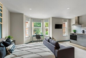 A modern bedroom with a large bed, a desk, and a view of greenery. - Studio 4 in Coventry (Coventry)