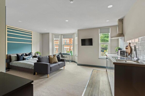 A modern hotel room with a bed, sofa, desk, and kitchenette. - Studio 4 in Coventry (Coventry)