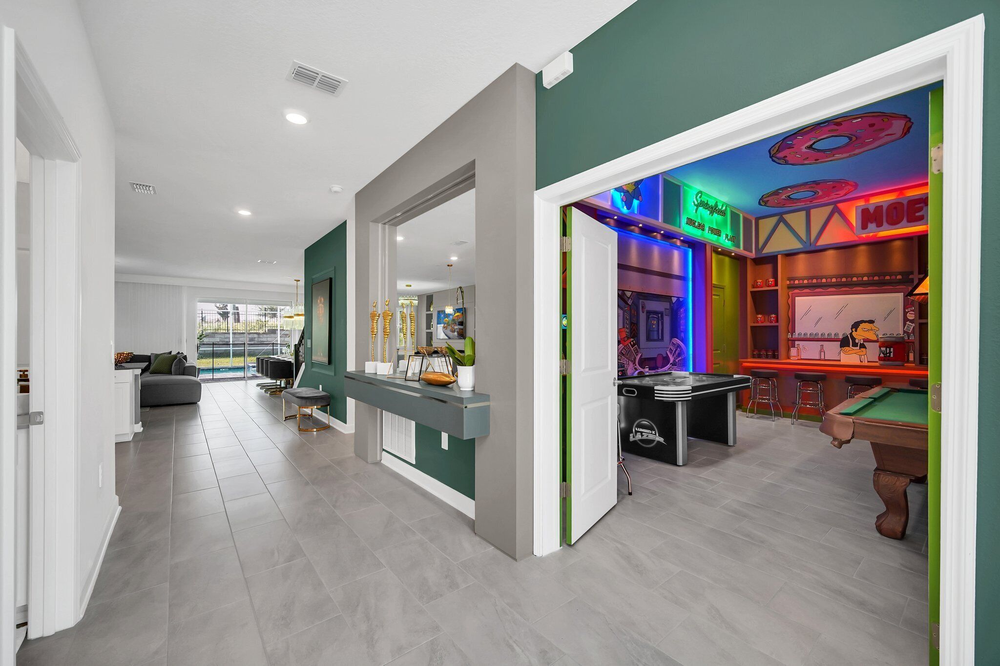 A modern interior with a reception desk, a pool table, and a bar area with neon signs.