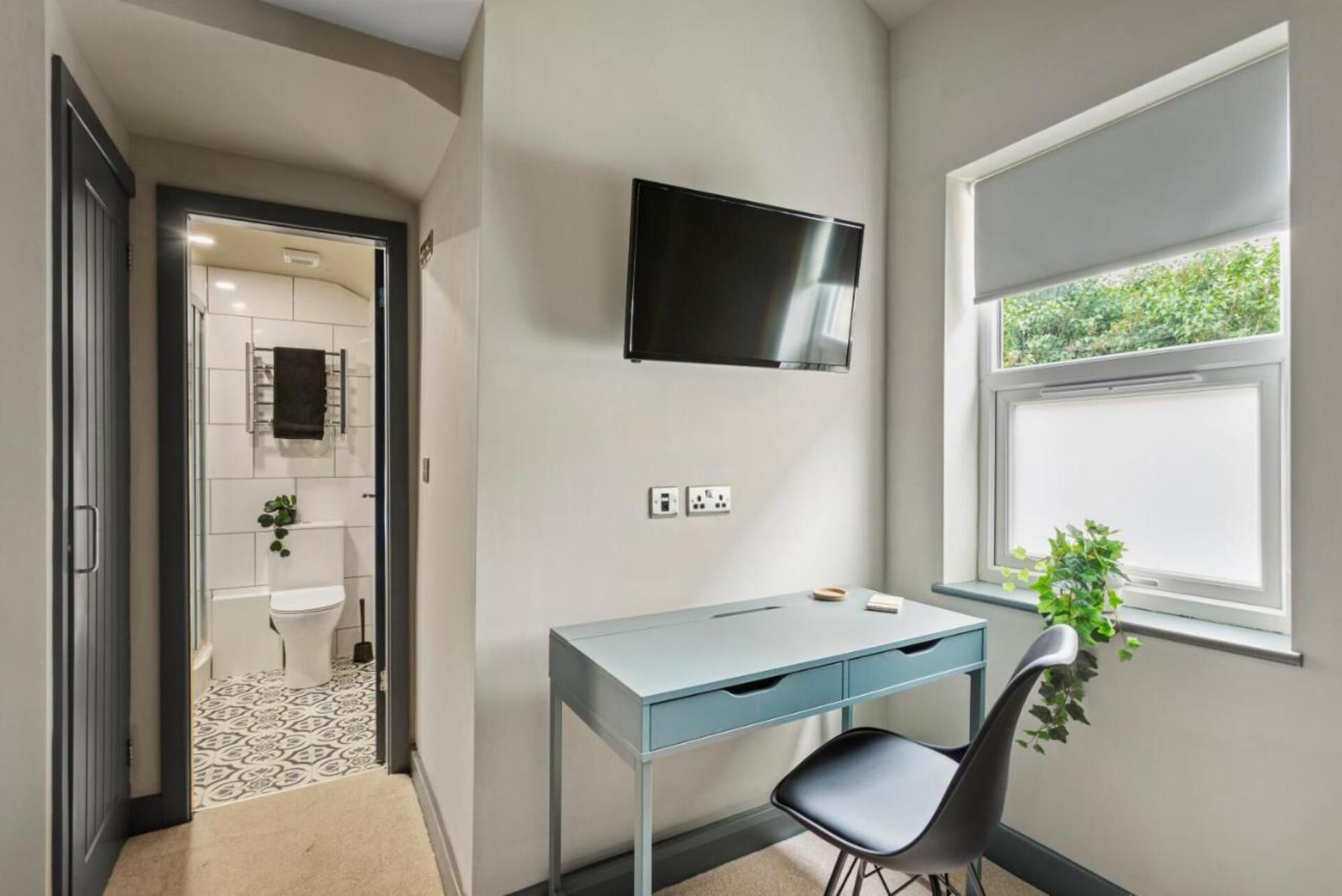 Quarto moderno com escrivaninha, cadeira e televisão fixada na parede.