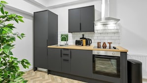 A modern kitchen with dark cabinets, a wooden countertop, a built-in oven, and a stainless steel range hood. - Studio 8 in Nottingham (Nottingham)