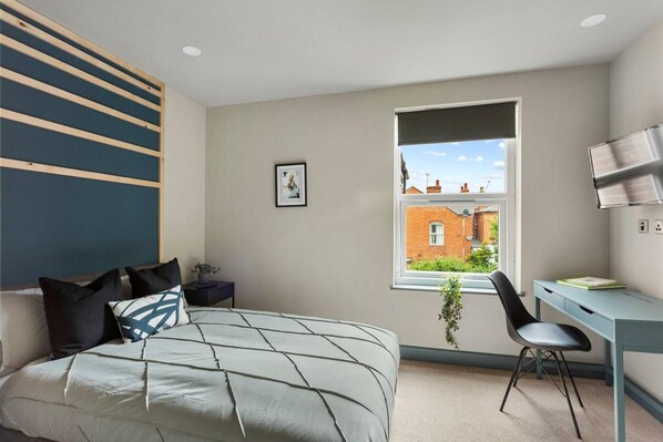 A bedroom with a bed, a desk, and a window with a view of a brick building. - Room 5 25 Meriden Street (Coventry)