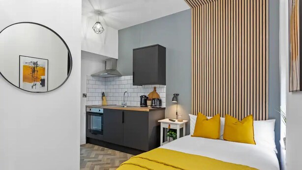 A modern hotel room with a bed, a bedside table, a lamp, and a view of the kitchen. - Studio 5 in Nottingham (Nottingham)