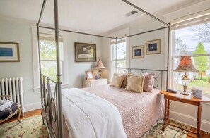Classic bedroom with a four-poster bed, bedside table, and large window offering a view of the outdoors.