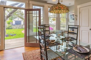 Enjoy meals in this dining area with a glass table and modern chairs, surrounded by a beautiful outdoor space with a lawn and deck.