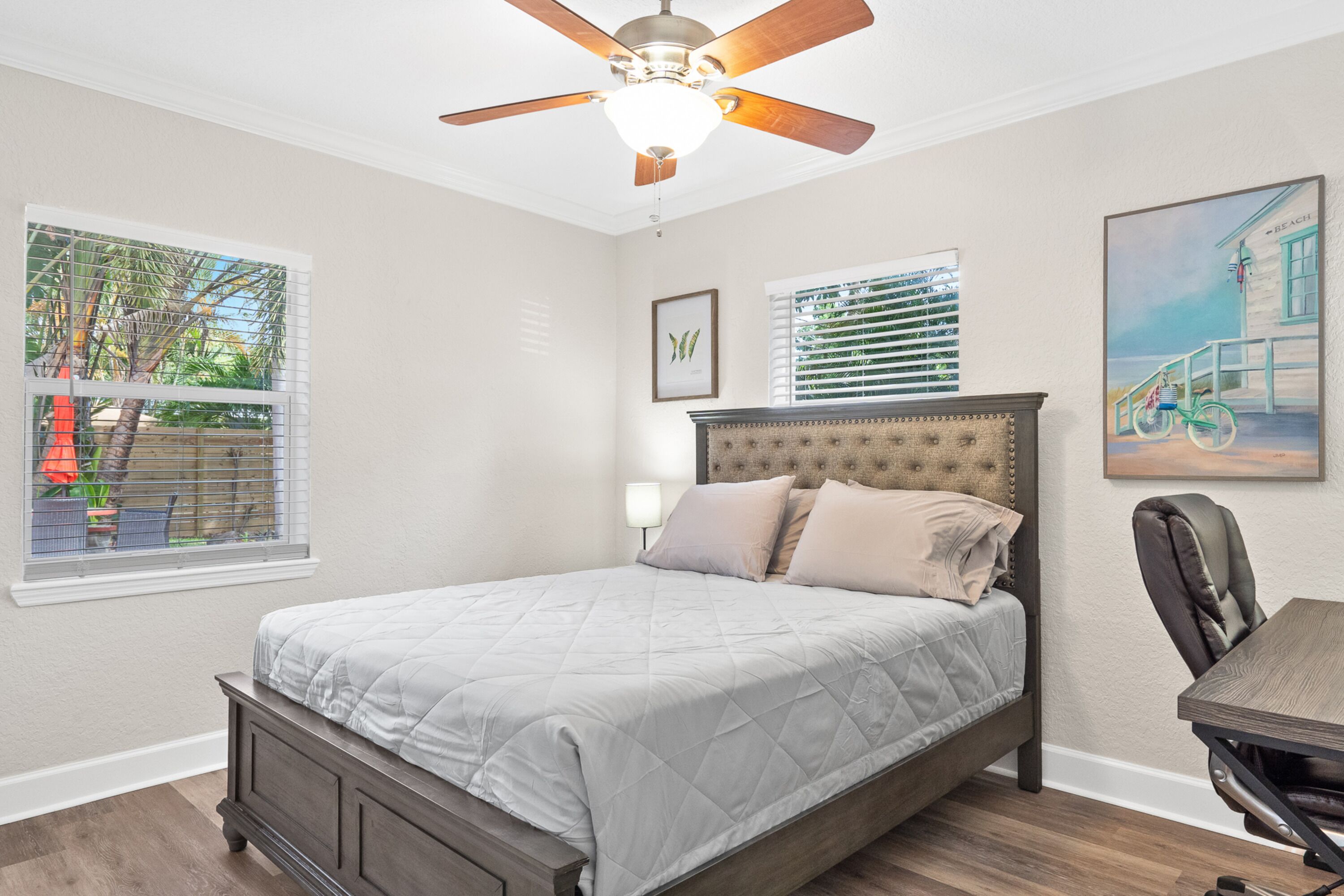 A bedroom with a bed, a ceiling fan, and a painting on the wall.