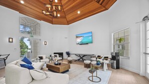 Ein geräumiges Wohnzimmer mit hoher Decke, einem großen an der Wand montierten Fernseher, einem bequemen Sofa, einem Couchtisch und einem Essbereich mit Tisch und Stühlen.