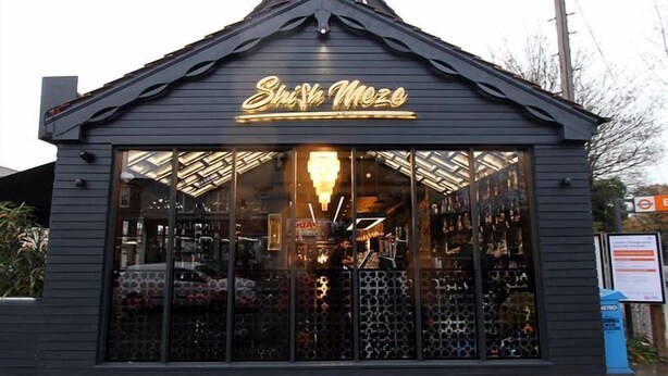 A building with a sign reading "Shisha Mezo" and large windows displaying various items inside. - Stylish 3-bed House in Hornchurch - Free Parking (Hornchurch)