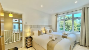 A hotel room with a large bed, two bedside tables, a window with a view of greenery, and a staircase with a railing. - Stylish 3-bed House in Hornchurch - Free Parking (Hornchurch)