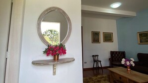 Un salon avec un grand miroir rond, une petite table sur laquelle est posé un vase de fleurs, un canapé et un fauteuil.