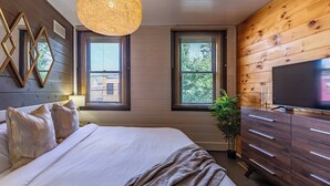 Ein Schlafzimmer mit einem Bett, einem Fernseher, Holzwänden und zwei Fenstern mit Jalousien.