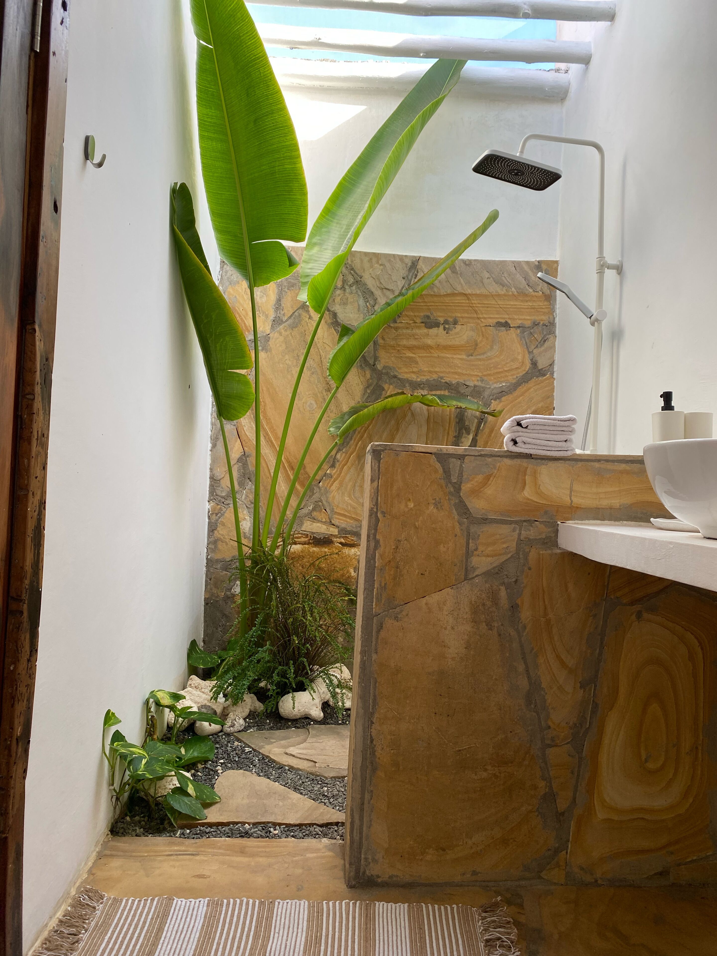 Une salle de bain avec un mur en pierre, une douche, un lavabo avec un bac blanc et un porte-serviettes.