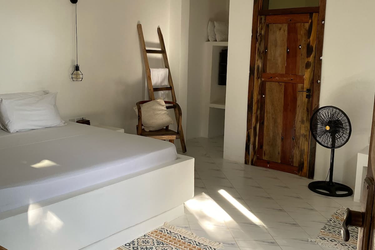Un dormitorio con una cama, una escalera de madera, un ventilador y una alfombra estampada.