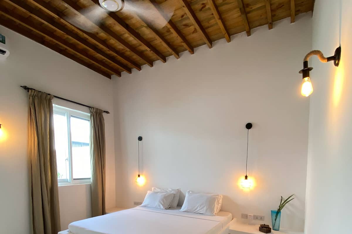 Un dormitorio con una cama grande, vigas de madera en el techo, un ventilador de techo y dos lámparas fijadas a la pared.