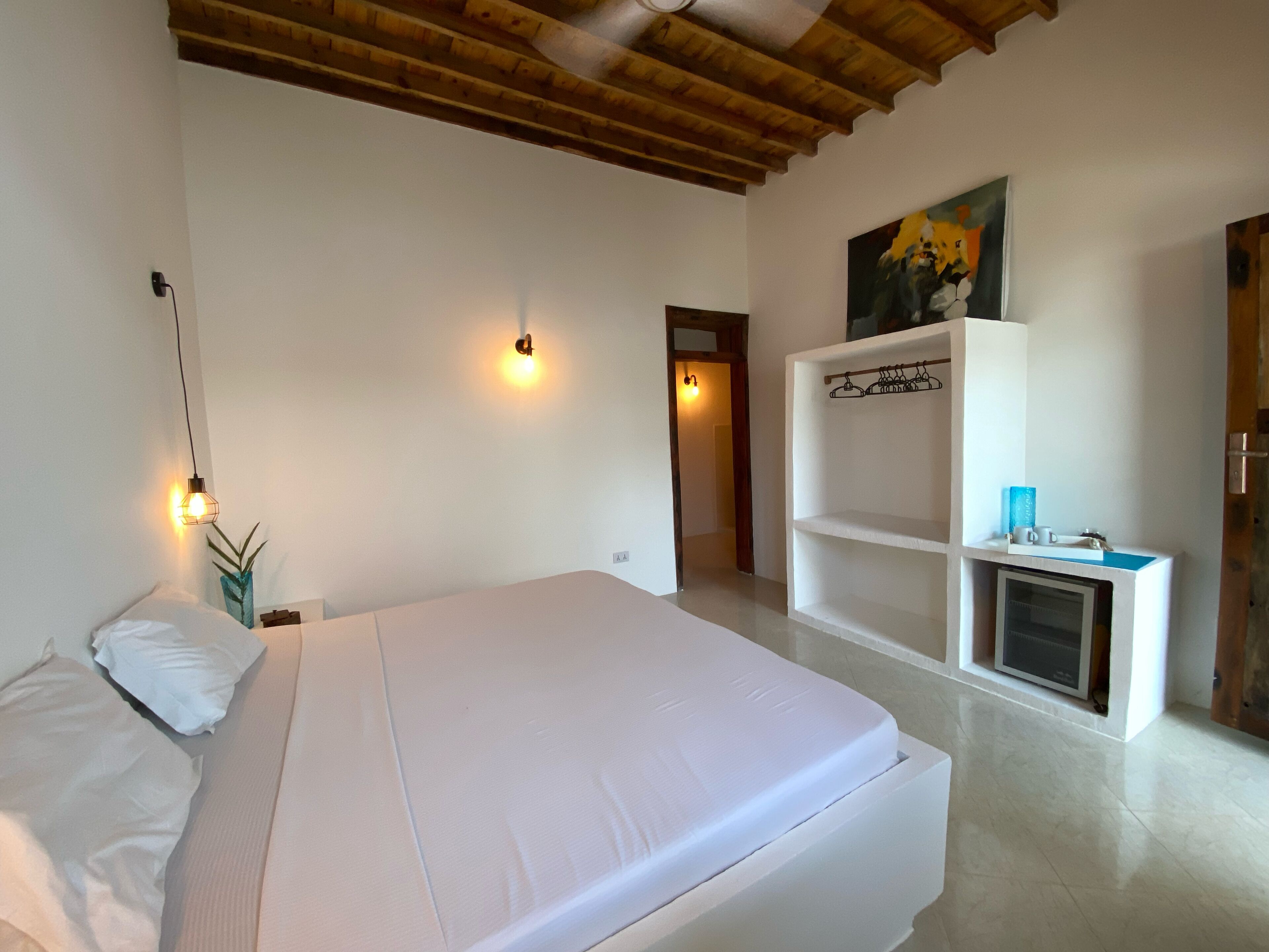 Un dormitorio con una cama, un estante con televisor y un cuadro en la pared.