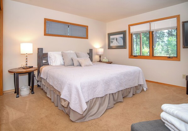 A bedroom with a large bed, two bedside tables, a window with blinds, and a framed picture on the wall.