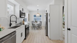 A modern kitchen with white cabinetry, a black faucet, a built-in oven, and a dining area with a table and chairs. - 250 steps to the Beach | Heated pool + spa (Holmes Beach)