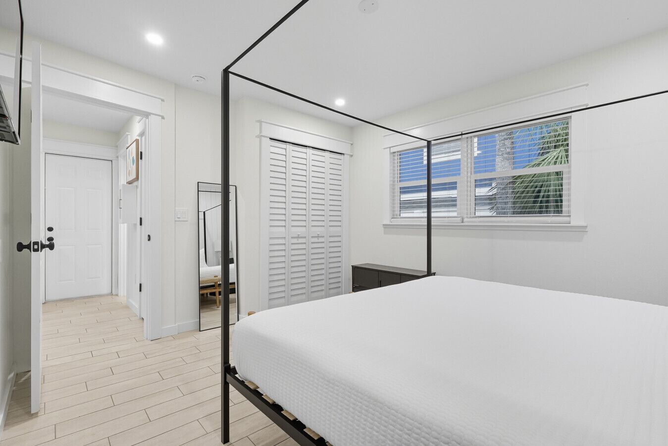 Un dormitorio con cama, ventana con persianas, puerta y espejo.