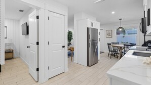 Une cuisine moderne avec des meubles blancs, un réfrigérateur en acier inoxydable et un coin repas comprenant une table et des chaises.